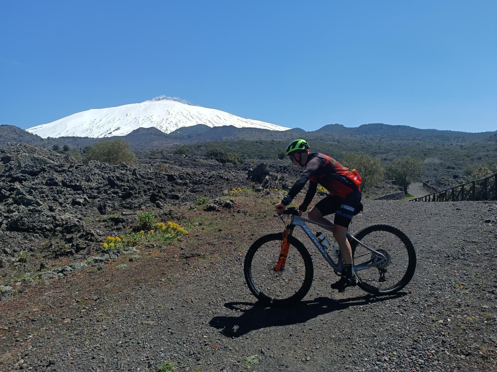 Un ciclista sulla pista tra le colate laviche, con la cima dell'Etna innevata sullo sfondo